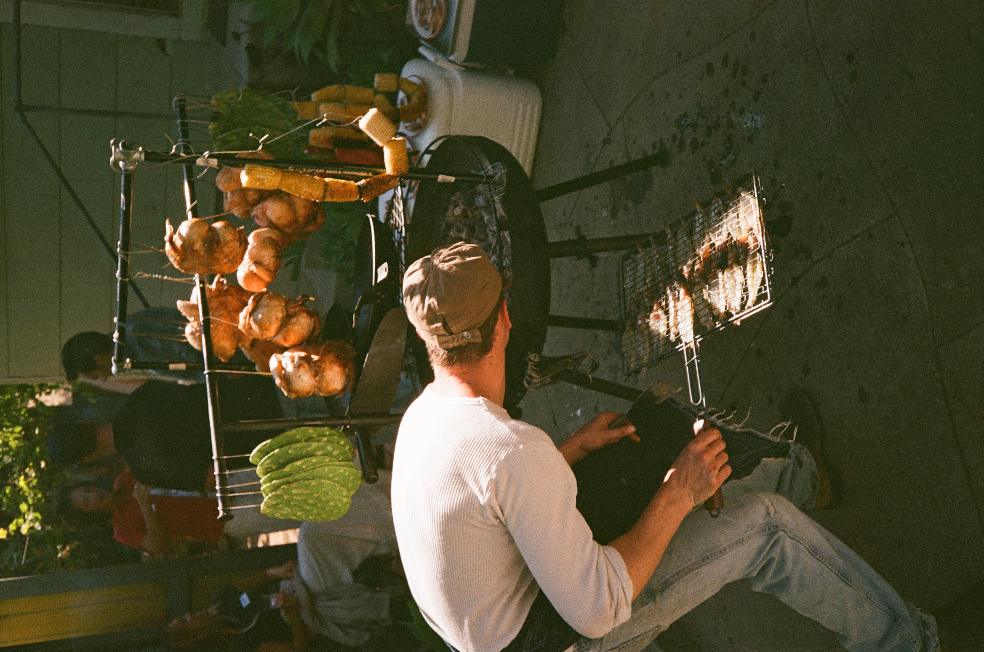 Zack checking the grill beneath hanging chickens and vegetables