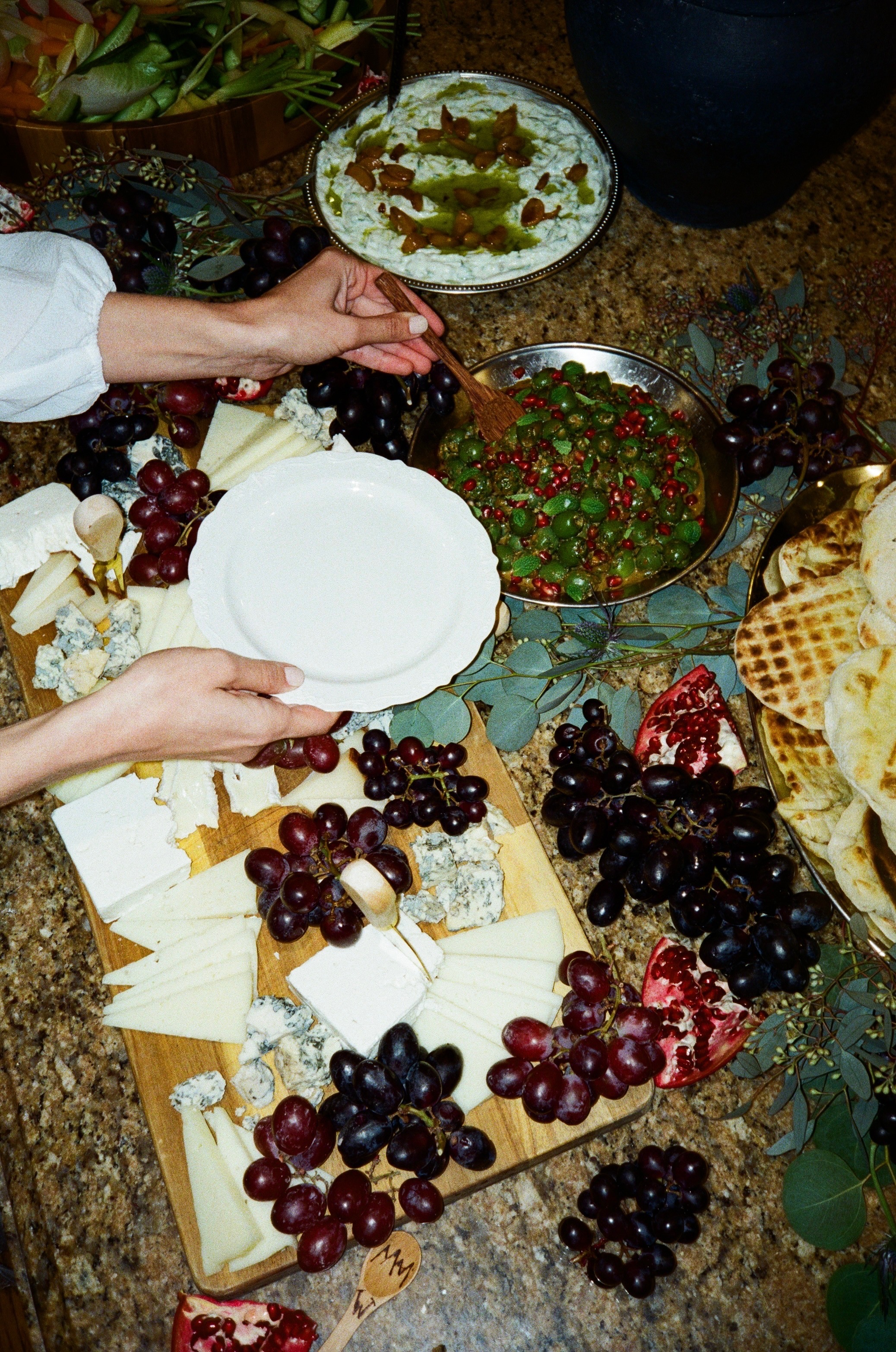 A generous event table of cheeses, olives, grapes, and flatbread